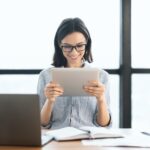 young girl holding tablet and using laptop at office - Digital Web Nova